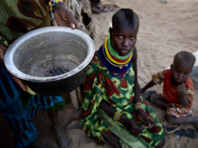 A Turkan woman holds up an empty pot in front of her two children